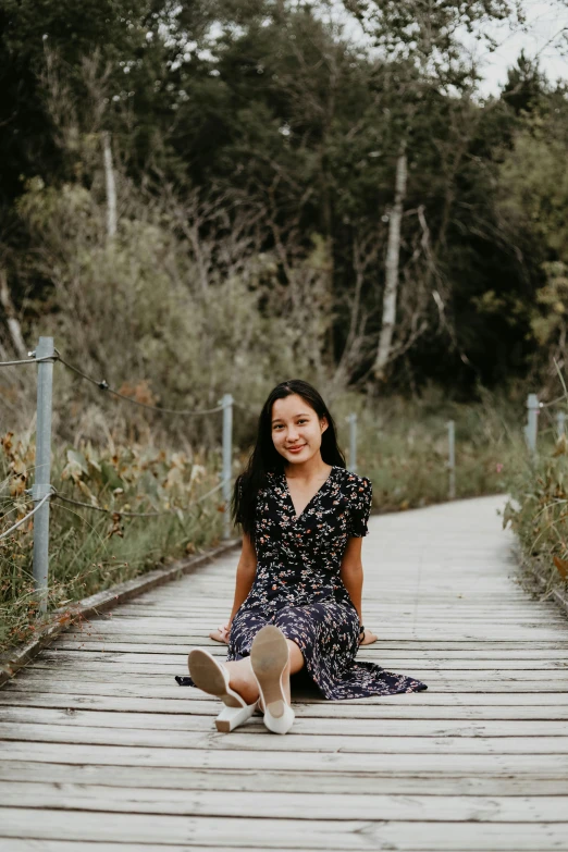 a woman sitting on top of a wooden walkway, a picture, inspired by helen huang, unsplash, happening, happily smiling at the camera, wearing a dress, low quality photo, female with long black hair