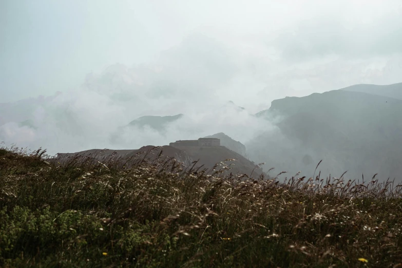 a person standing on top of a grass covered hillside, by Attila Meszlenyi, unsplash contest winner, romanticism, rain and smoke, ruins around, light grey mist, craggy