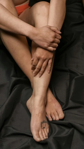 a woman sitting on a bed with her legs crossed, inspired by Victorine Foot, pexels, antipodeans, on black background, holding each other hands, skin texture natural, gray men