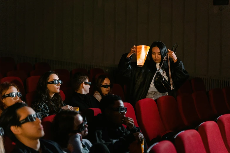 a group of people sitting in a theater watching a movie, a hologram, by Julia Pishtar, trending on pexels, hyperrealism, digital sunglasses, holding a pair of fans. unreal 5, rick owens, fall season