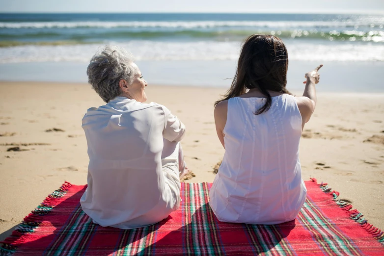 two women sitting on a blanket on the beach, by Arabella Rankin, pexels contest winner, symbolism, two old people, having a picnic, looking onto the horizon, slide show