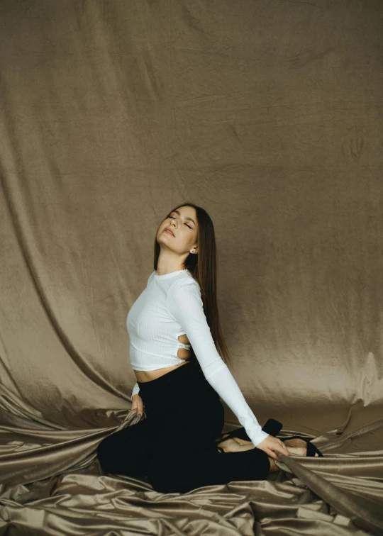 a woman sitting on a bed in a white top and black pants, an album cover, inspired by Elsa Bleda, pexels contest winner, arabesque, profile pose, on a velvet table cloth, low quality photo, promotional image