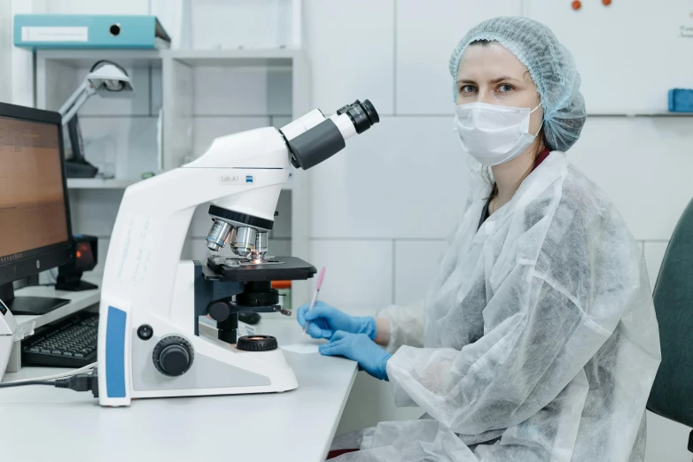 a woman in a lab coat using a microscope, a microscopic photo, by Adam Marczyński, shutterstock, surgical gown and scrubs on, avatar image, instagram photo, uhq