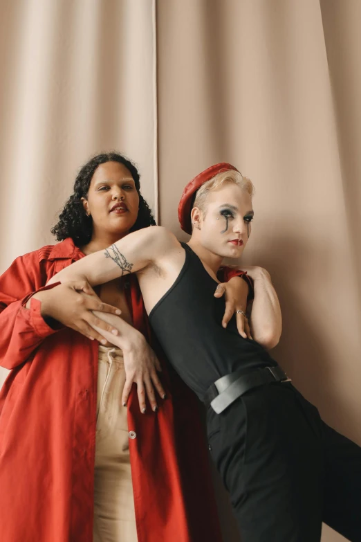 a couple of women standing next to each other, an album cover, inspired by Nan Goldin, trending on pexels, renaissance, non-binary, plus-sized, wearing red clothes, mix of ethnicities and genders