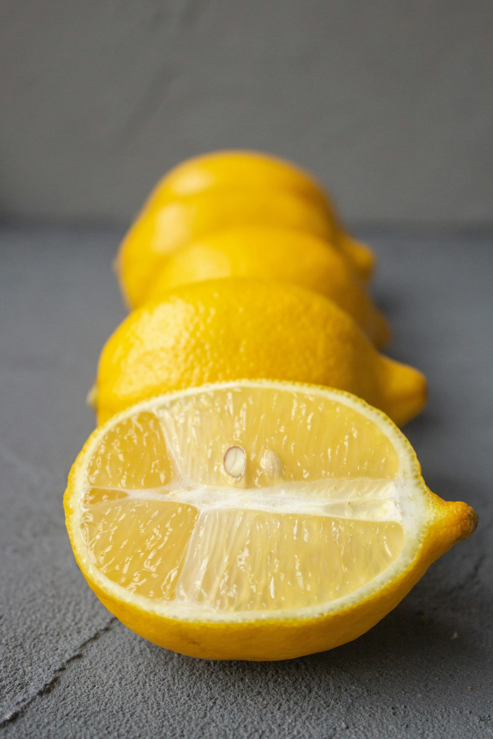 a group of lemons sitting on top of a table, detailed product image, on a gray background, licking out, side lights