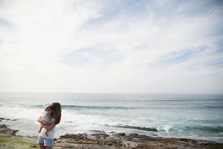 a couple of people standing on top of a rocky beach, bulli, with a kid, hugging, lots of ocean