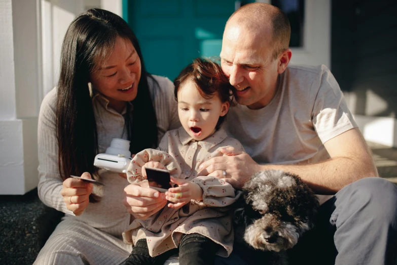 a man sitting next to a woman and a child, pexels contest winner, happening, she is holding a smartphone, avatar image, asian descent, playing