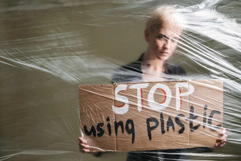 a woman standing in the water holding a sign, unsplash, plasticien, plastic and fabric, plaster, a blond, recycled