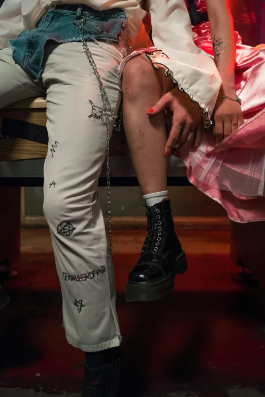 a man and a woman sitting on a bench, a tattoo, inspired by Nan Goldin, trending on pexels, renaissance, white pants, close-up on legs, punk party, [ theatrical ]