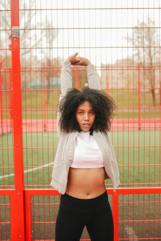 a woman posing for a picture in front of a fence, pexels contest winner, happening, sport bra and shirt, afro tech, square, on a soccer field