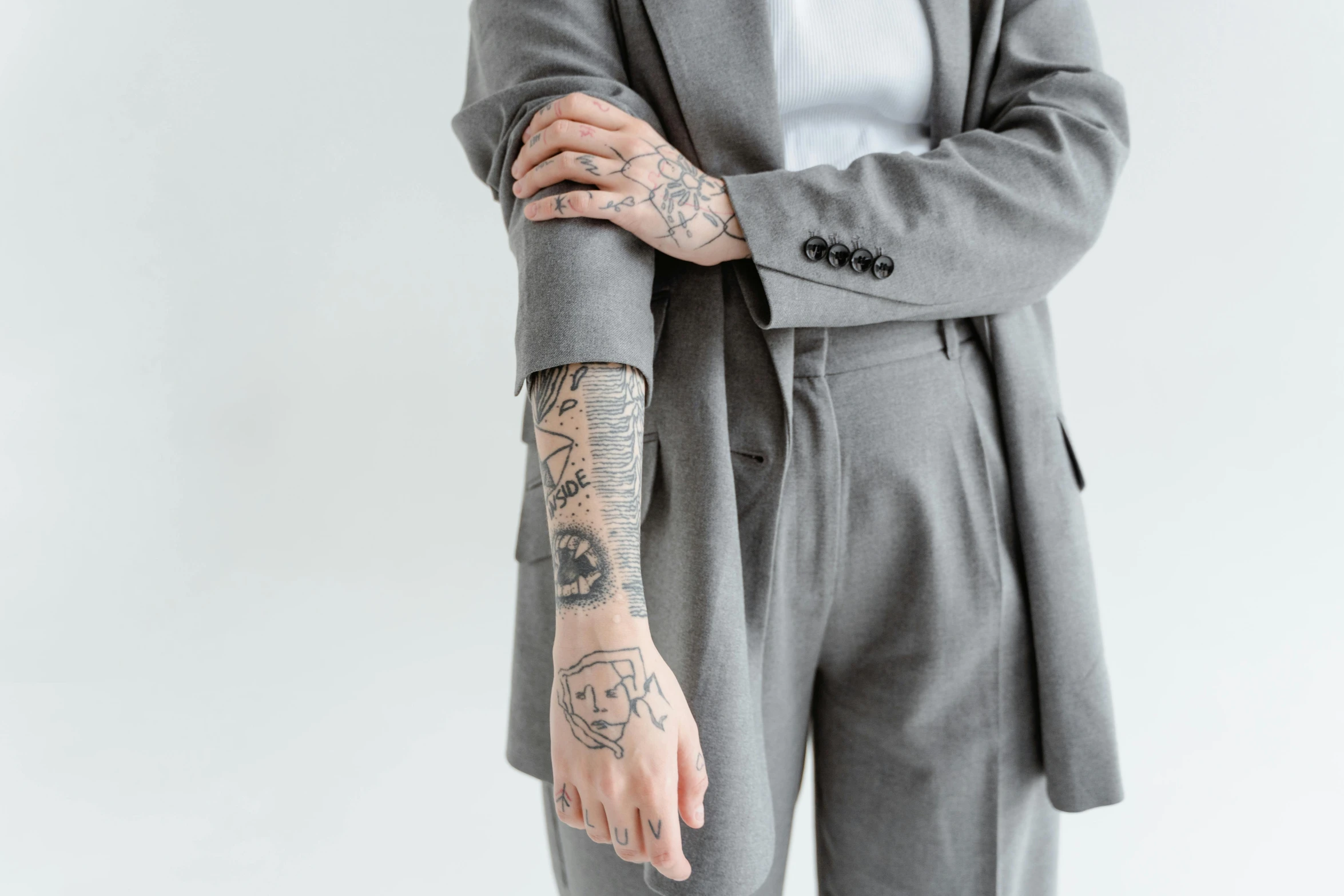 a woman with a tattoo on her arm, inspired by Mathieu Le Nain, trending on pexels, grey suit, set against a white background, arms covered in gang tattoo, office clothes