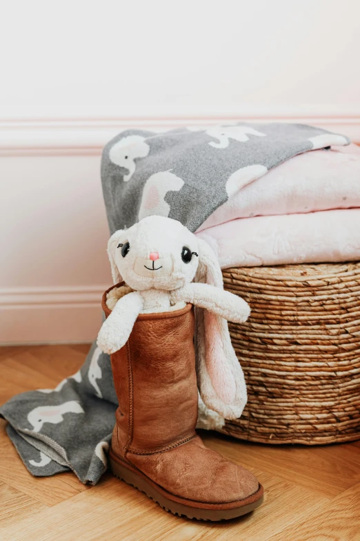 a pair of brown boots sitting on top of a wooden floor, the bunny has pink fur, covered with blanket, jellycat, throw