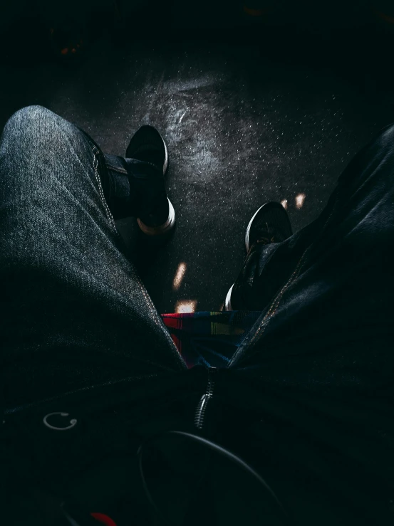 a person standing in the dark with their feet up, an album cover, trending on unsplash, realism, jean and multicolor shoes, taken on go pro hero8, siting in a chair, looking down from above