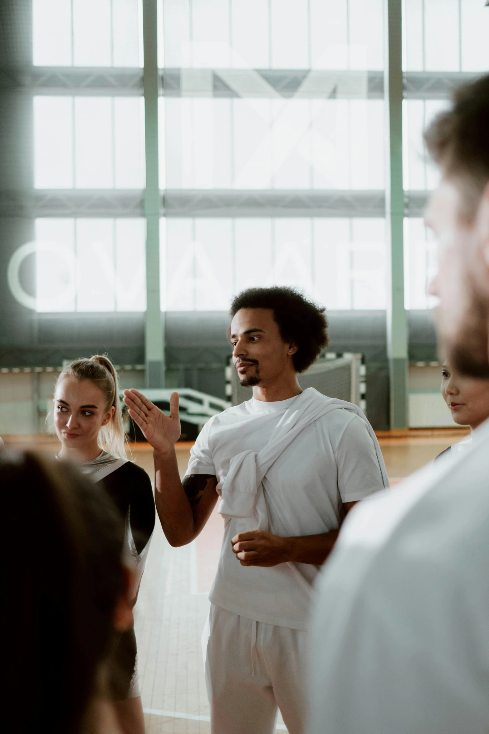 a group of people standing around each other, in a gym, black man with afro hair, teaching, jovana rikalo