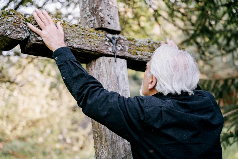 a man standing next to a wooden cross, unsplash, an elderly, touching tree in a forest, profile image, jimmy page