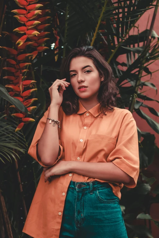 a woman standing in front of a plant talking on a cell phone, an album cover, trending on pexels, wearing an orange t shirt, pokimane, wearing a linen shirt, portrait mode photo