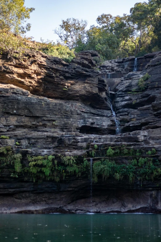 a waterfall in the middle of a lush green forest, les nabis, shiny layered geological strata, manuka, terraced, rocky cliff