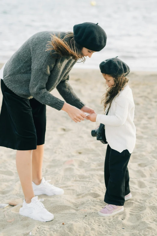 a woman standing next to a little girl on a beach, by Lucia Peka, unsplash, renaissance, beanie, holding paws, on the sand, fancy dressing