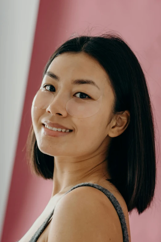a woman standing in front of a pink wall, a character portrait, by helen huang, clean face and body skin, beauty mark on cheek, smiling and looking directly, square jaw-line