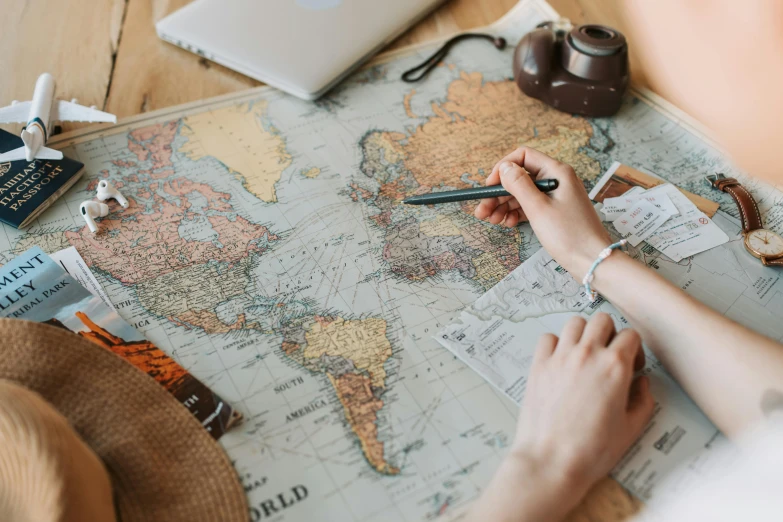 a woman sitting at a table writing on a map, trending on pexels, crafts and souvenirs, uk, group photo, all these worlds are yours