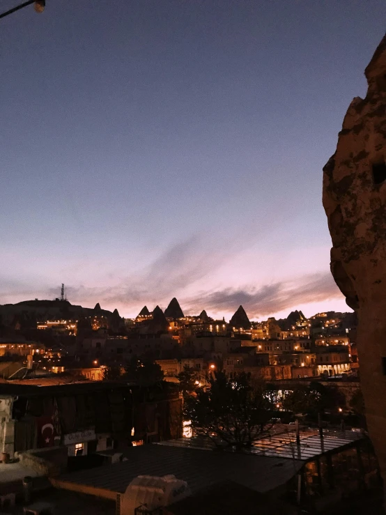 a view of a town lit up at night, buildings carved out of stone, during sunrise, epic land formations, cozy