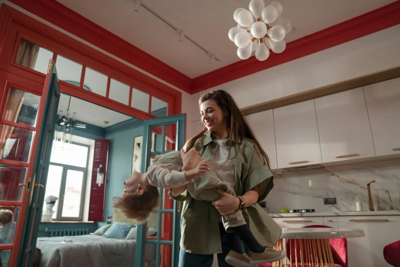 a woman holding a baby in her arms, pexels contest winner, altermodern, things hanging from ceiling, inside a cozy apartment, red and teal color scheme, joyful people in the house