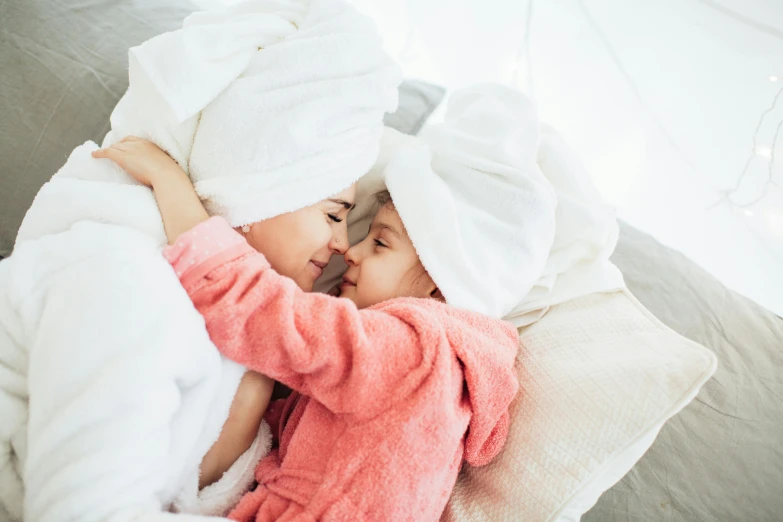 a couple of kids laying on top of a bed, by Emma Andijewska, pexels contest winner, happening, bathrobe, skincare, hugging, fully covered