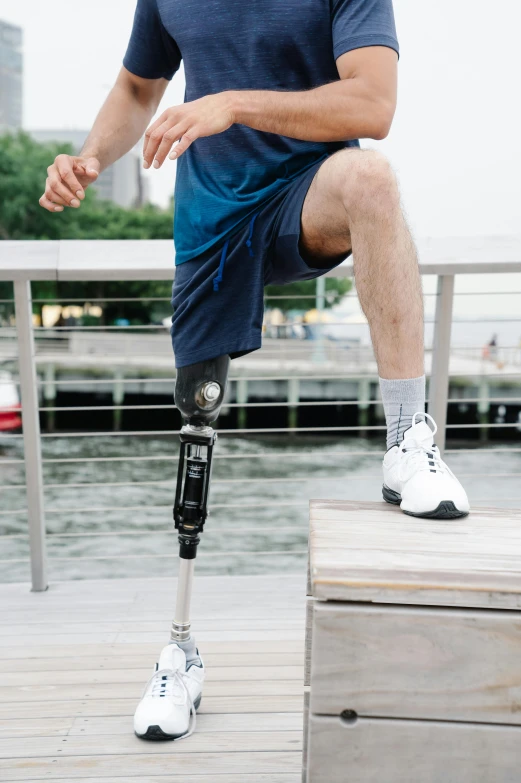 a man sitting on top of a wooden platform next to a body of water, prosthetic leg, power implants, harbor, instagram post