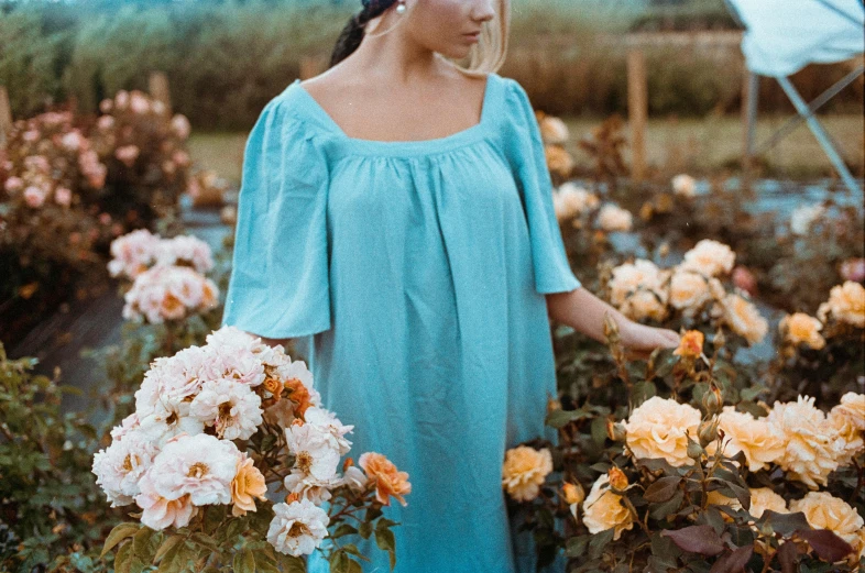 a woman standing in a field of flowers, inspired by Pierre Puvis de Chavannes, pexels contest winner, romanticism, teal tunic, square, rose garden, light blue