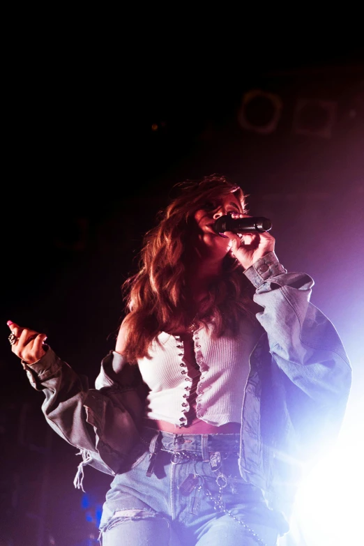 a woman standing on top of a stage holding a microphone, by Robbie Trevino, pexels, renaissance, bella thorne, say ahh, yawning, low light