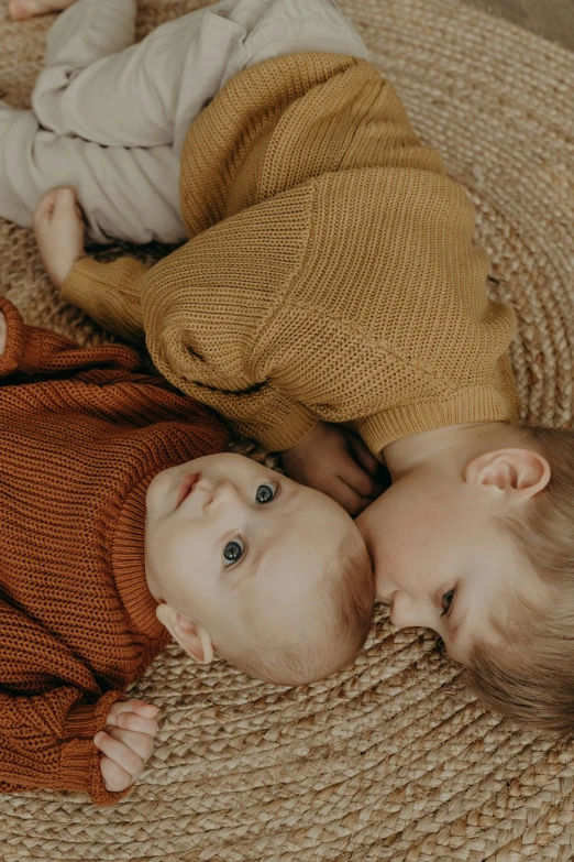 a couple of babies laying on top of a rug, unsplash contest winner, ocher details, sweater, zoomed in, full colour