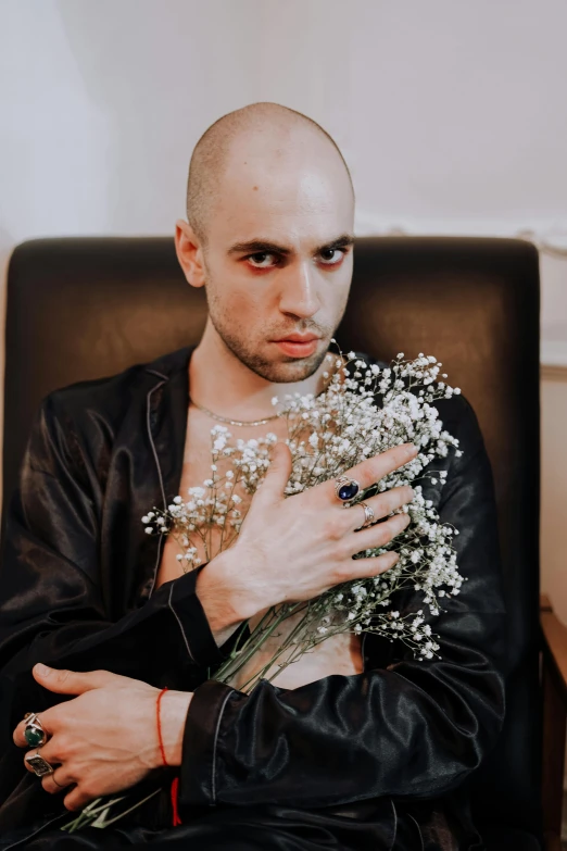 a man sitting in a chair holding a bunch of flowers, an album cover, inspired by Elsa Bleda, unsplash, antipodeans, bald male swashbuckler, wearing studded leather, beautiful young man, hasbulla magomedov