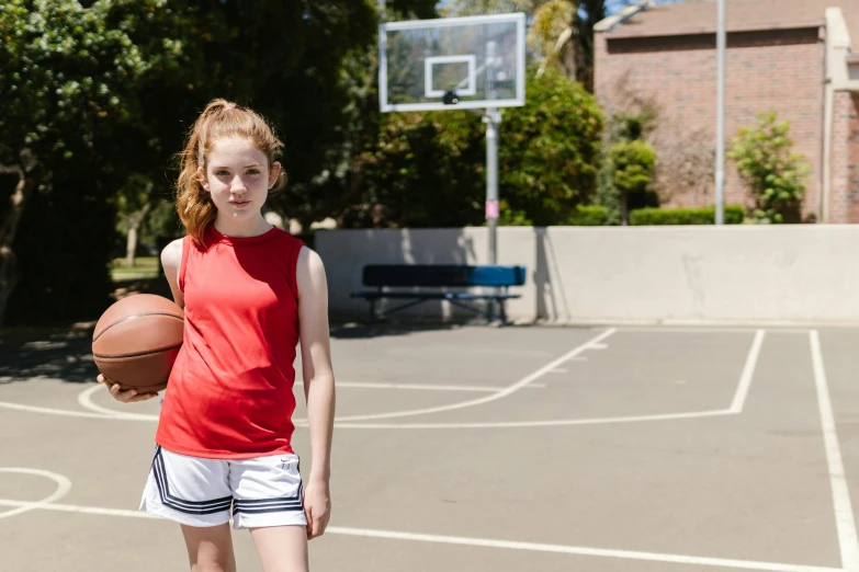 a girl standing on a basketball court holding a basketball, by Gavin Hamilton, dribble contest winner, 15081959 21121991 01012000 4k, ellie bamber, sport shorts, school courtyard