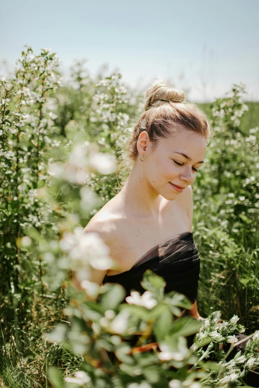 a woman sitting in a field of flowers, an album cover, by Sara Saftleven, an elegant woman in black dress, portrait of elle fanning, candid portrait photo, hair styled in a bun