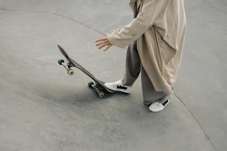 a man riding a skateboard up the side of a ramp, pexels contest winner, hyperrealism, wearing a long beige trench coat, wearing white sneakers, on a gray background, woman is curved