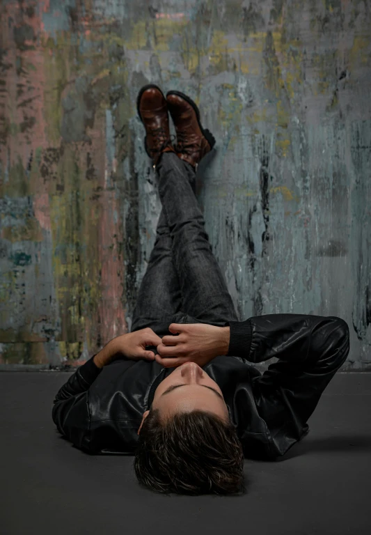 a man laying on the ground with his feet up, an album cover, trending on pexels, conceptual art, she wears leather jacket, frank dillane, peter hurley, trending on artstion