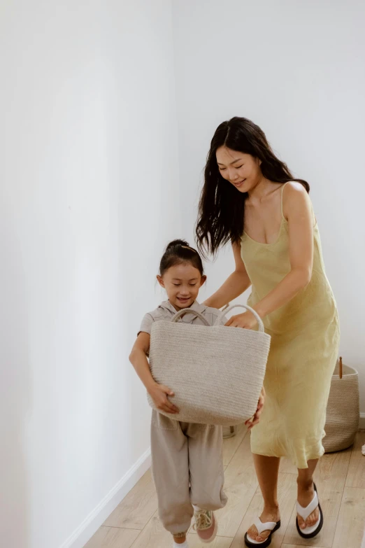 a woman standing next to a little girl holding a pillow, inspired by Li Di, pexels contest winner, minimalism, with an easter basket, beige, asian descent, linen