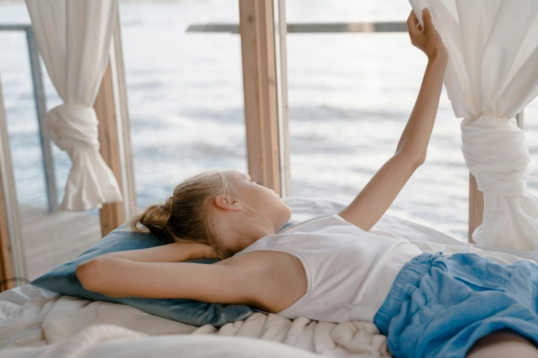 a woman laying on top of a bed next to a window, pexels contest winner, happening, holding a book, relaxing at the beach, pictured from the shoulders up, girls resting