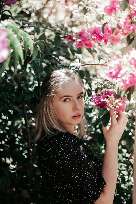 a woman standing in front of a bush of flowers, unsplash, realism, portrait of kim petras, medium format. soft light, abcdefghijklmnopqrstuvwxyz, tourist photo