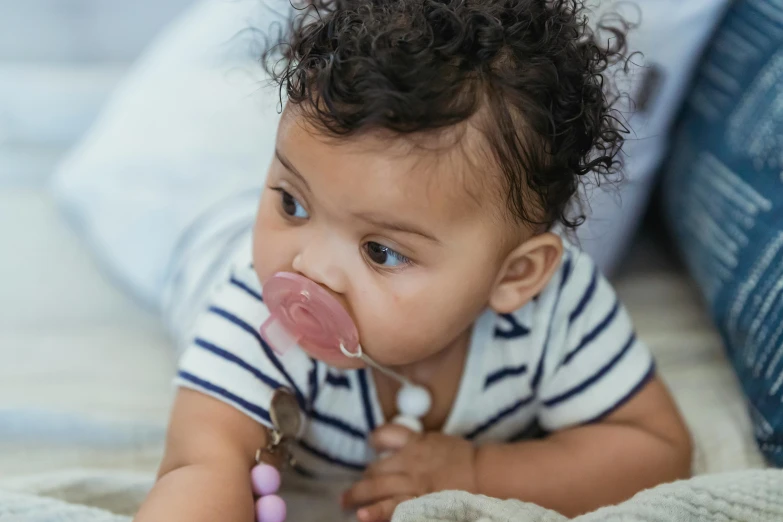 a baby laying on a bed with a pacifier in its mouth, by Nina Hamnett, pexels contest winner, happening, mixed race, putting on lipgloss, at home, close up shot from the side