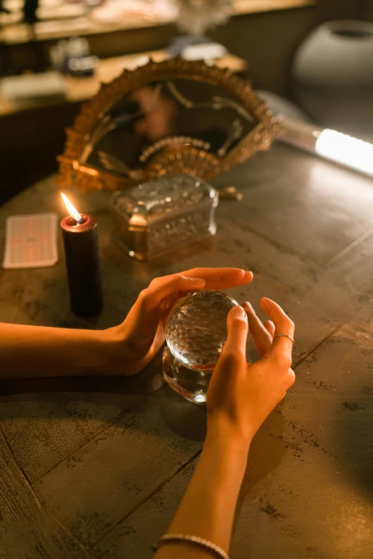 a person sitting at a table with a candle, a hologram, trending on pexels, magical realism, holding a crystal ball, hands reaching for her, apothecary, afternoon lighting