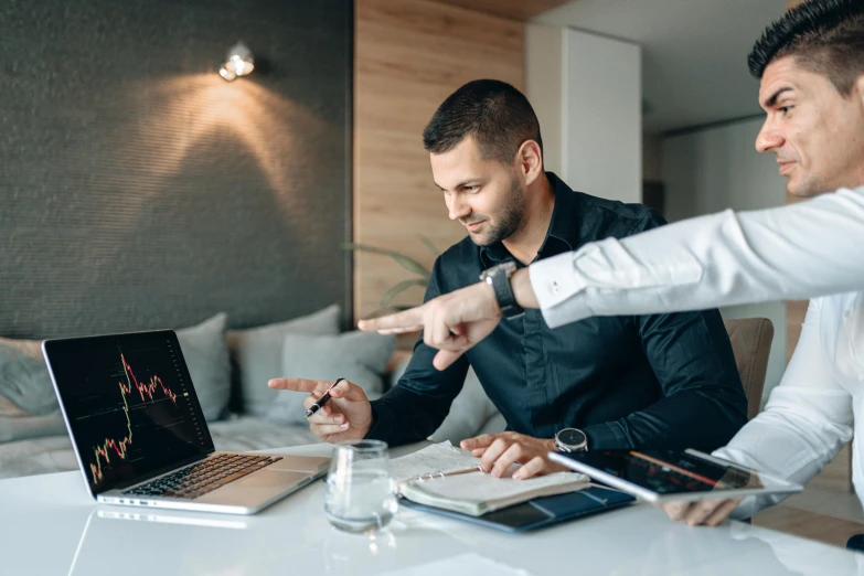 two men sitting at a table looking at a laptop, by Adam Marczyński, pexels contest winner, wearing business casual dress, with pointing finger, lachlan bailey, charts