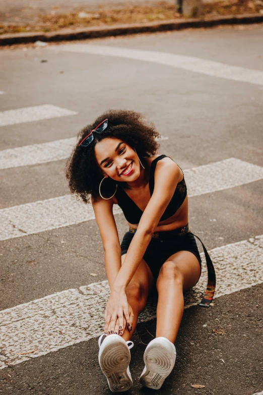 a woman sitting on the ground in front of a crosswalk, pexels contest winner, tight black tank top and shorts, curly afro, smiling confidently, trending photo