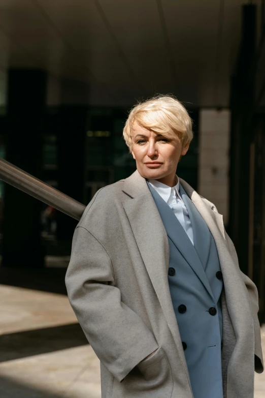 a woman standing on a sidewalk in front of a building, inspired by Cindy Sherman, trending on pexels, lawyer suit, short platinum hair tomboy, in london, portrait of rugged adult female