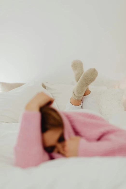a woman laying on top of a bed covered in a pink blanket, trending on pexels, wearing casual sweater, overknee socks, contemplating, gif