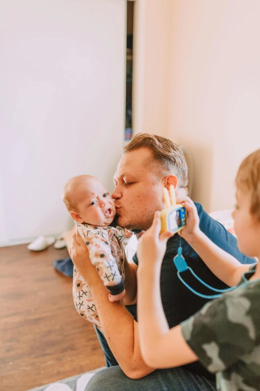 a man sitting on the floor holding a baby, a picture, pexels contest winner, kissing together, toy camera, headshot, caspar david