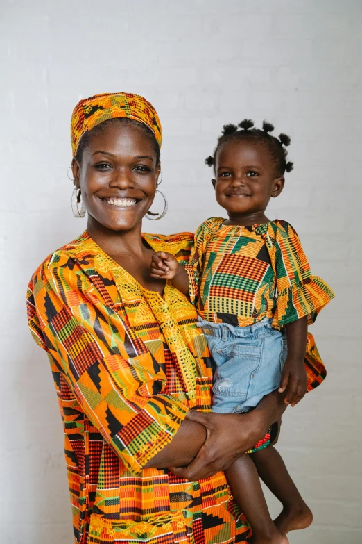 a woman holding a child in her arms, pexels contest winner, afrofuturism, wearing an african dress, both smiling for the camera, mango, wide frontal view