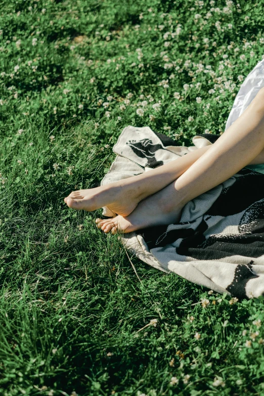 a woman sitting on a blanket in the grass, unsplash, happening, foot wraps, ignant, high - contrast, carefully crafted