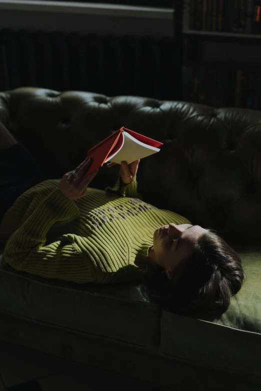 a woman laying on a couch reading a book, inspired by Elsa Bleda, wearing a green sweater, jonny greenwood, **cinematic, shot with sony alpha