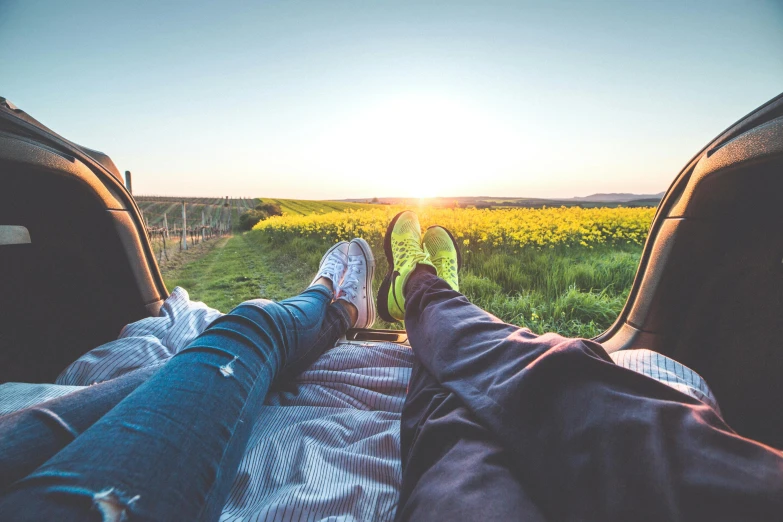 a couple of people sitting in the back of a car, pexels contest winner, bare feet in grass, looking onto the horizon, at sunrise in springtime, laying down